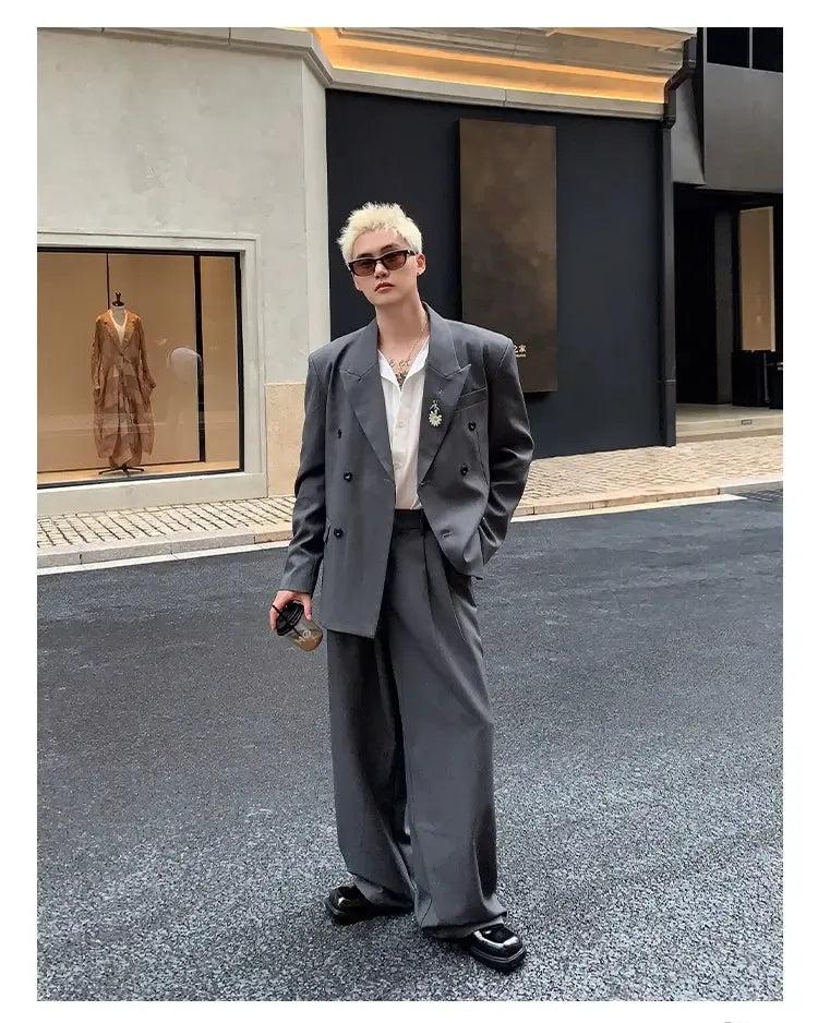 A person wearing a gray suit and sunglasses stands on a street, with a storefront visible in the background.