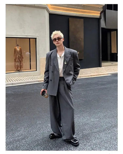 A person wearing a gray suit and sunglasses stands on a street, with a storefront visible in the background.