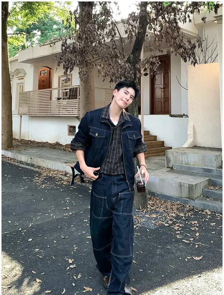 A young man wearing a denim jacket and jeans is walking on a street, smiling and holding a drink.