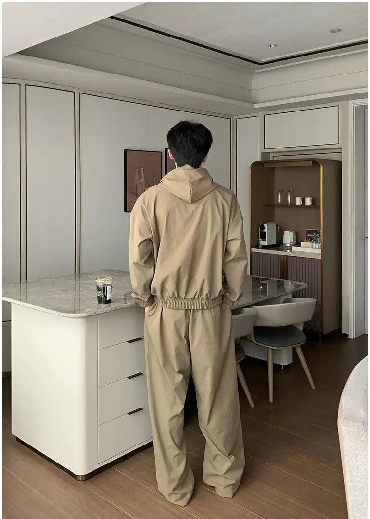 A person in a beige hoodie stands in a modern kitchen, facing away from the camera.