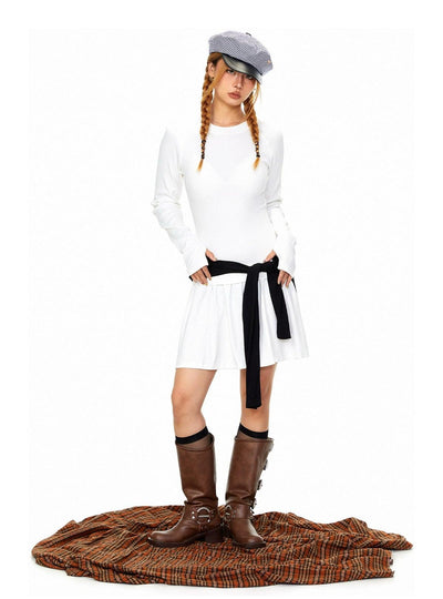 A woman wearing a white dress, a gray hat, and brown boots stands on a brown and orange plaid blanket.
