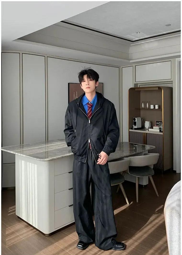 A man in a black suit stands in a modern kitchen with a marble countertop and a wooden cabinet.