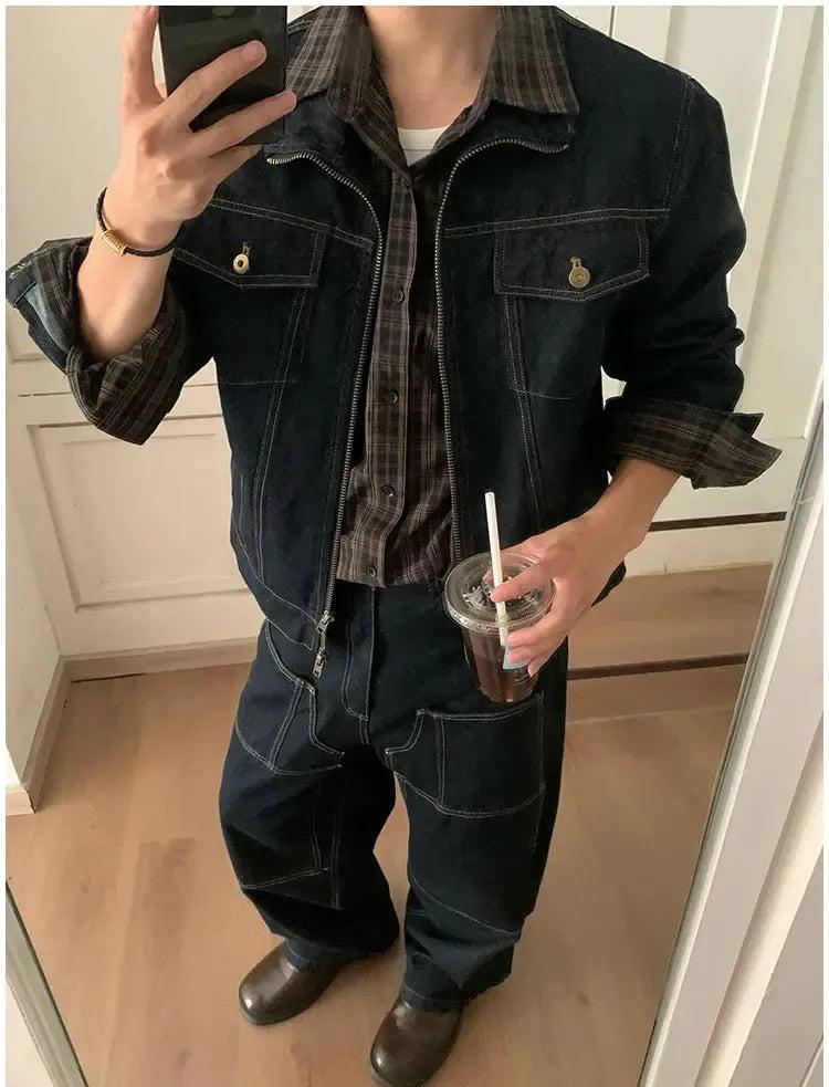 A person is taking a selfie in a mirror, wearing a denim jacket, plaid shirt, and jeans, while holding a drink in a cup.